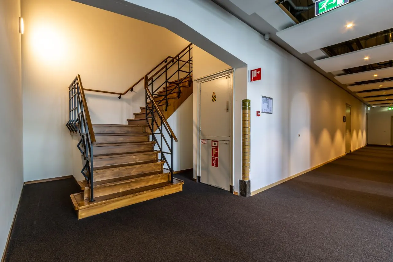 Trapopgang met houten treden en zwart metalen leuning naast een gang in een kantoorpand aan de Lage Naarderweg.